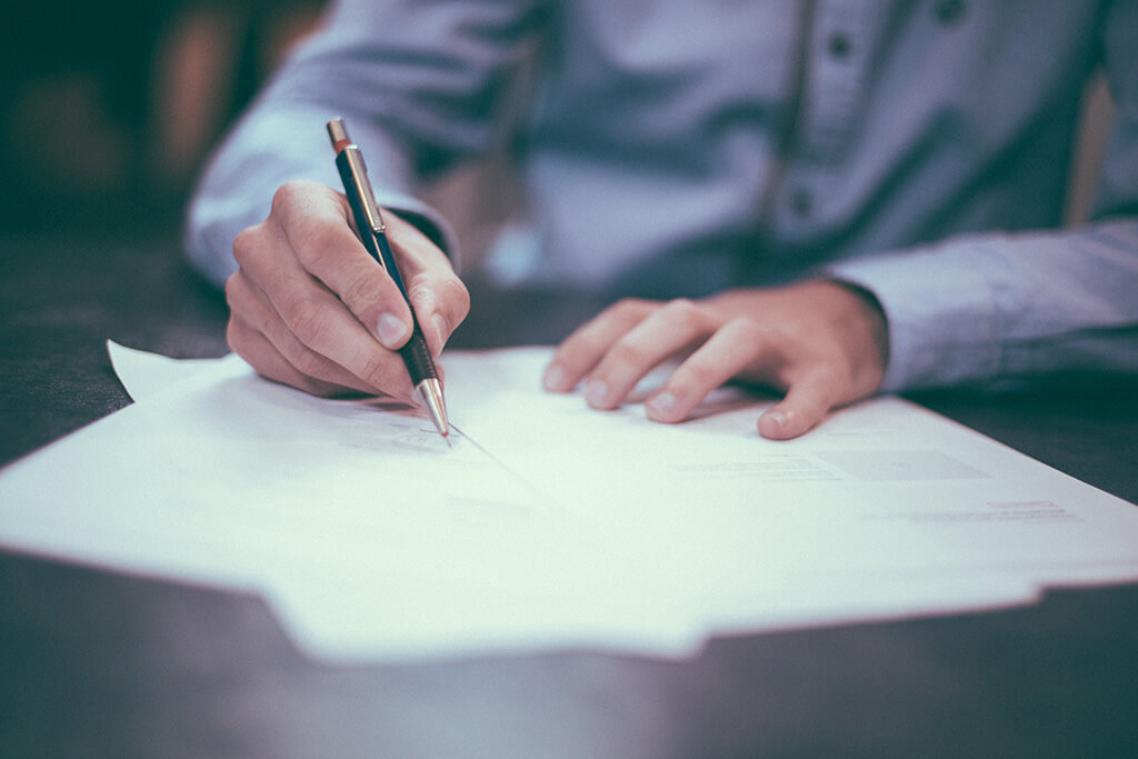 Image of a man wearing a white button down shirt and writing on a document
